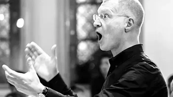 En bald mand med briller taler udholdende og har hænderne i luften.