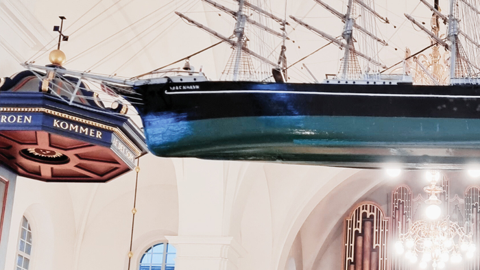 En stor skibsmodell hænger i et højt og belyset hall.