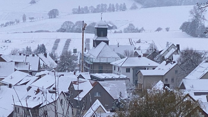 Schneebedecktes Dorf mit einem markanten Gebäude in der Mitte, umgeben von Feldern und Bäumen.