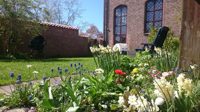 En smuk have med blomster og en rød murstensbygning i baggrunden