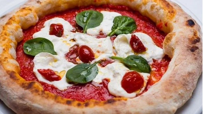 En frisk pizza med mozzarella, tomater og spinat.