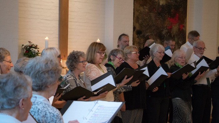 En kor sang i kirke med blæselys og blomster.