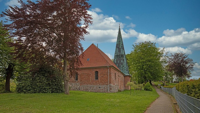 Kleine Kirche mit hohem Turm auf grünem Rasen bei klarem Himmel