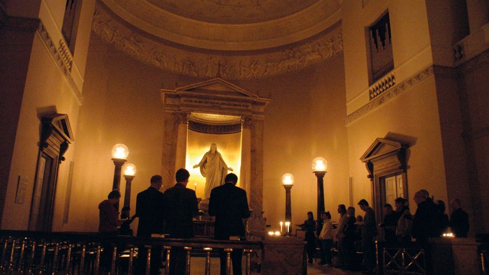 En kirkeindendoms interiør med lysende lys og en gruppe mennesker i bænkene.