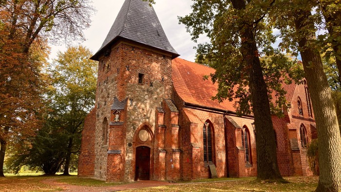 Alte Kirche aus rotem Backstein umgeben von Bäumen