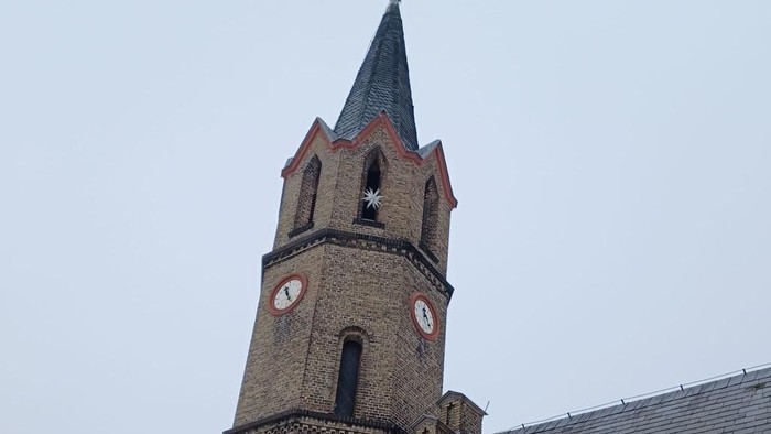 Kirchturm mit Uhr und Spitze vor bewölktem Himmel