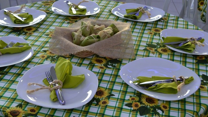 Ein festlich gedeckter Tisch mit weißen Tellern, grünen Servietten und silbernem Besteck auf einer Tischdecke mit Sonnenblumenmuster