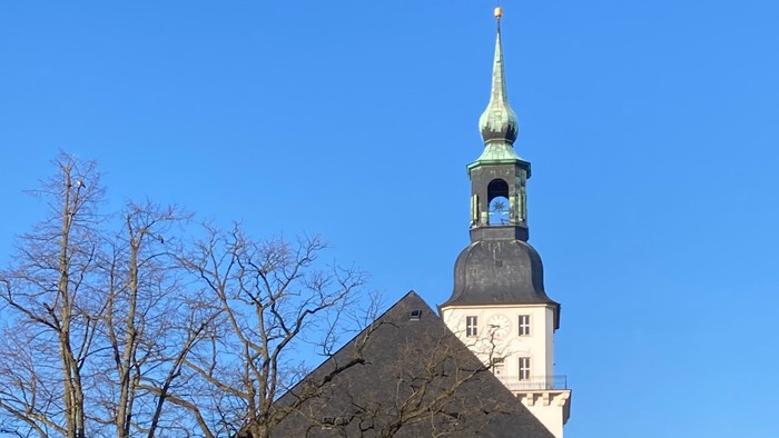 Weiße Kirche mit hohem Turm und grünem Dach unter blauem Himmel