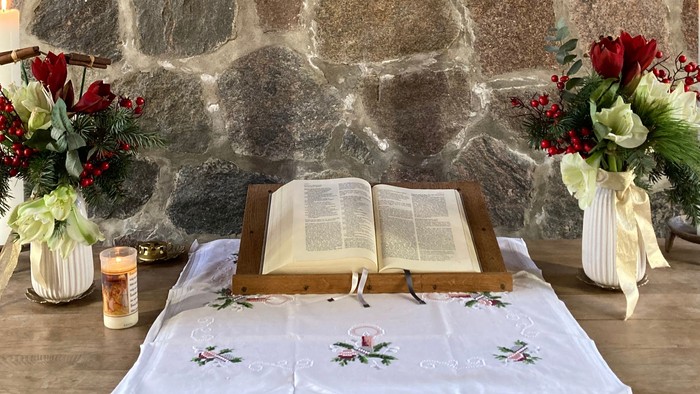 Ein Tisch mit offenem Buch, Kerzen und Blumen vor einer Steinwand