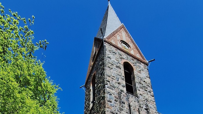 Gruppe von Menschen vor alter Kirche mit hohem Turm und blauen Himmel