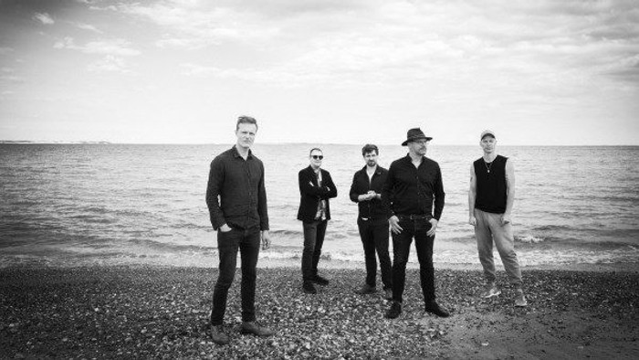 En gruppe mænd står på stranden.