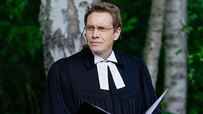 Außenaufnahme von Pastor Ralf Weisswange im Talar. Im Hintergrund Birken.