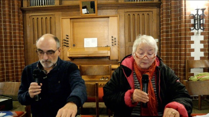 Zwei ältere Personen sitzen in einem Raum mit hölzerner Einrichtung und halten Mikrofone.