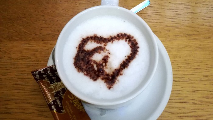 Eine Tasse Kaffee mit Herzmuster auf dem Schaum und ein Schokoladenriegel daneben