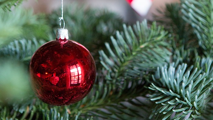 En rød glaskugle hænger på en julgran sammen med et hjerteformet pynt.