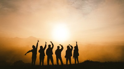 Eine Gruppe von Menschen feiert bei Sonnenuntergang auf einem Hügel.