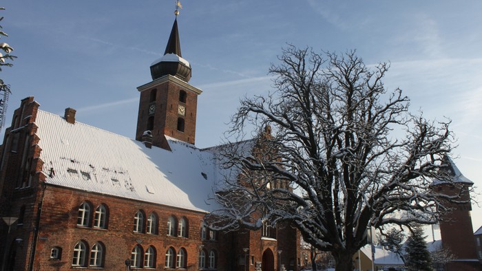 En snedækket kirke med tårn og en nakket træ foran