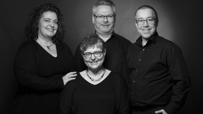 Vier Personen in Schwarz-Weiß-Fotografie, zwei Männer und zwei Frauen, lächeln in die Kamera