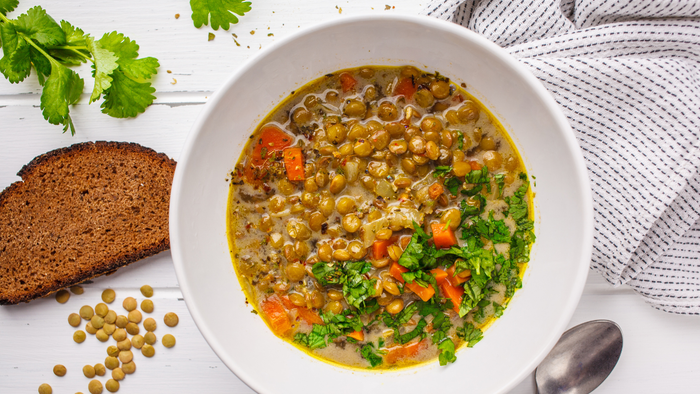 En bolle med linsensuppe med grønne æbler og kål, til stede er en skive rugbrød og en skønselt.