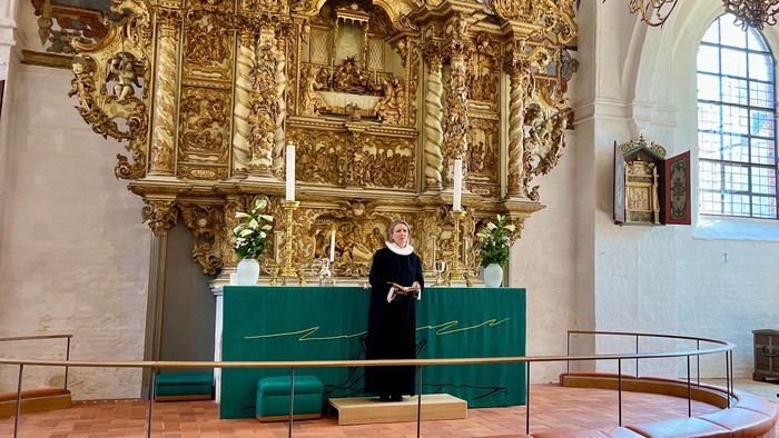 En præst i messeservice foretager tjeneste i en prægtig, gulddekoreret kirke.