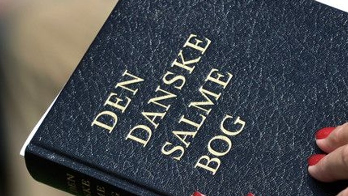 En hånd holder en Dansk Salmebog.