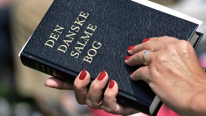 En hånd holder en Dansk Salmebog.