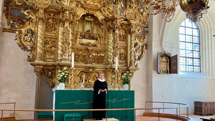 En præst i messeservice foretager tjeneste i en prægtig, gulddekoreret kirke.