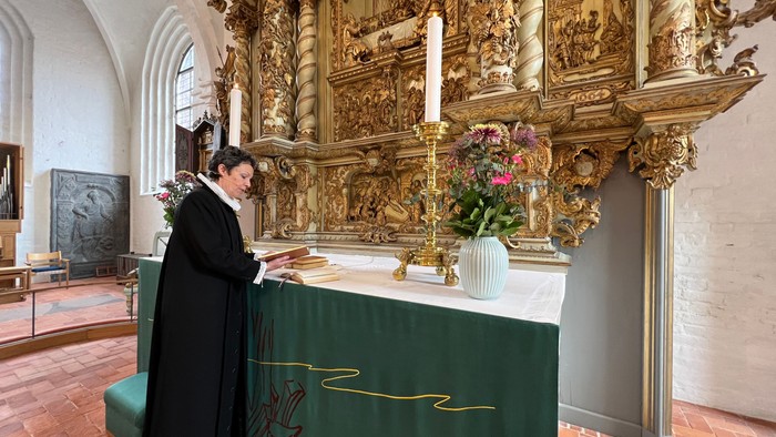 Mand i mørkt tøj står ved alter i prægtig kirke med gulddekor.