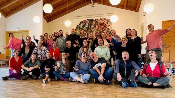 Eine große Gruppe von Menschen posiert in einem Raum mit Holzboden und Deckenlampen.