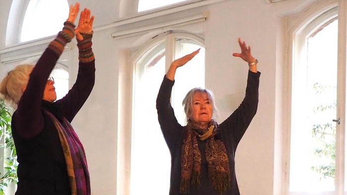 Zwei ältere Frauen üben Yoga in einem hellen Raum.