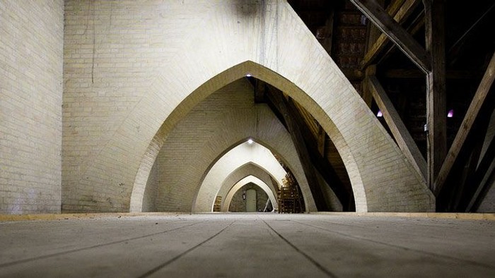 En mørk og smal gangway med bueformet indgang og ståltræger på væggen.