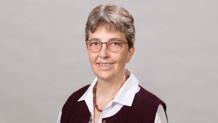 Eine Frau mit kurzem grauen Haar und Brille lächelt in die Kamera.