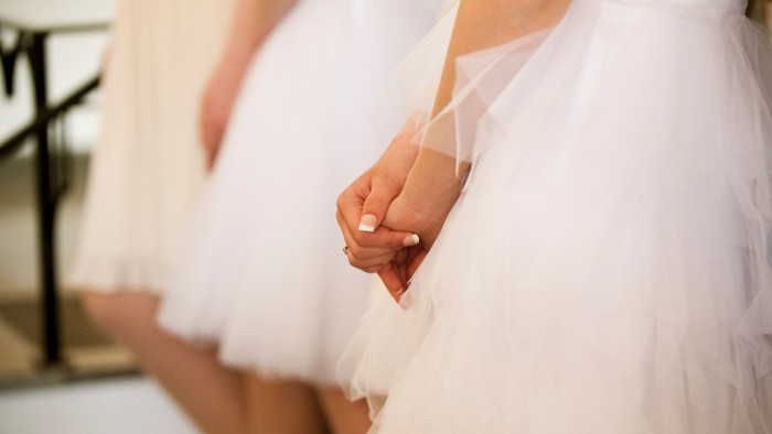 To brudepiger i hvide kledninger holder hånd.