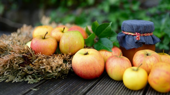 En samling æbler og en glass med marmelade på en trædeks.