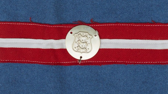 En stykke blå tøj med to røde og en hvid stribe, med et metalletiket med et motiv.