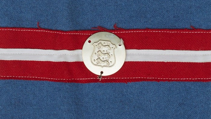 En stykke blå tøj med to røde og en hvid stribe, med et metalletiket med et motiv.