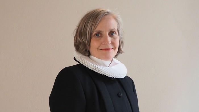 Kvinde i sort kaptajnmø, hvid krage og hvid kuffe.