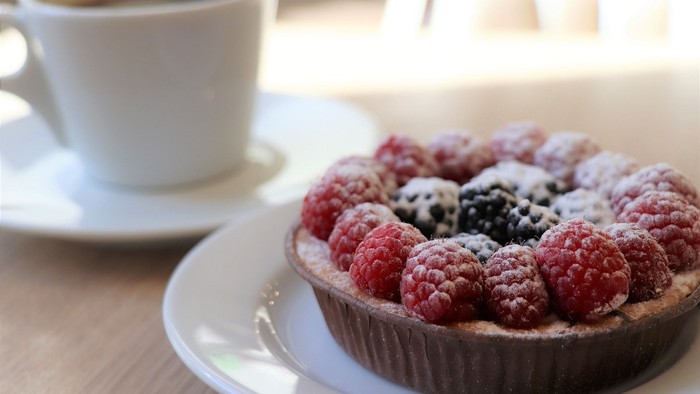 Ein Törtchen mit Beeren und ein Kaffee auf einem Tisch