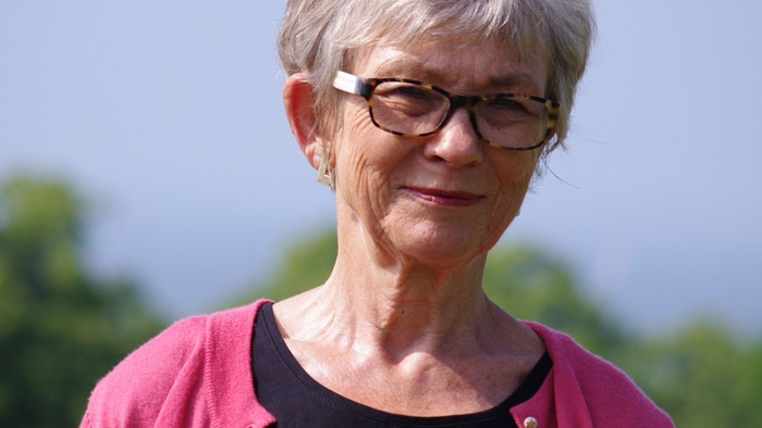 En kvinde med kort hår og briller, der bærer en rød cardigan og sort trøje.