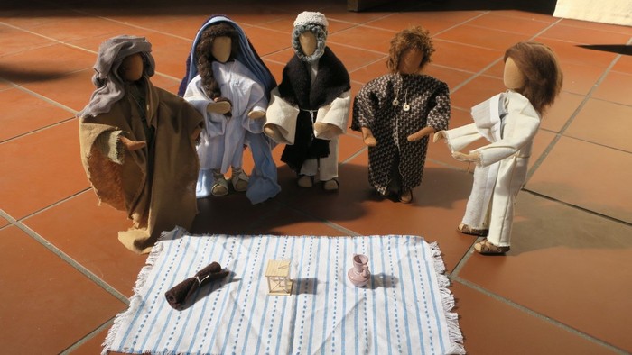 Fünf Puppen in traditioneller Kleidung um ein Tuch mit kleinen Gegenständen