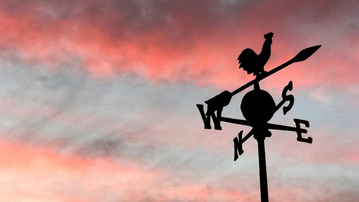 Ein Windfang mit Figur zeigt bei Sonnenuntergang die Windrichtung an