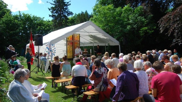 En gruppe mennesker sidder på bænke under et telt i en park og deltager i en udeaktivitet.