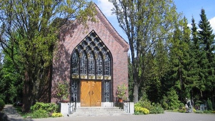 Kleine Kirche mit hohem, spitzem Eingang, umgeben von Bäumen und Büschen