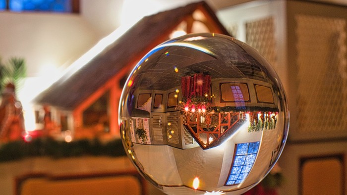 Ein Weihnachtsbaumschmuck reflektiert ein festlich dekoriertes Haus.