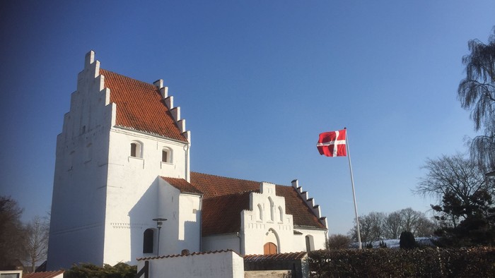Hvid kirke med spistegn og dansk flag på en klar dag