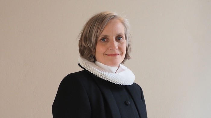 Kvinde i sort kaptajnmø, hvid krage og hvid kuffe.