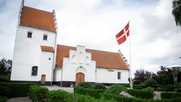 Hvid kirke med røde tag og dansk flag på tårn