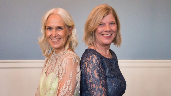 To kvinder står sammen og smiler til kameraet.