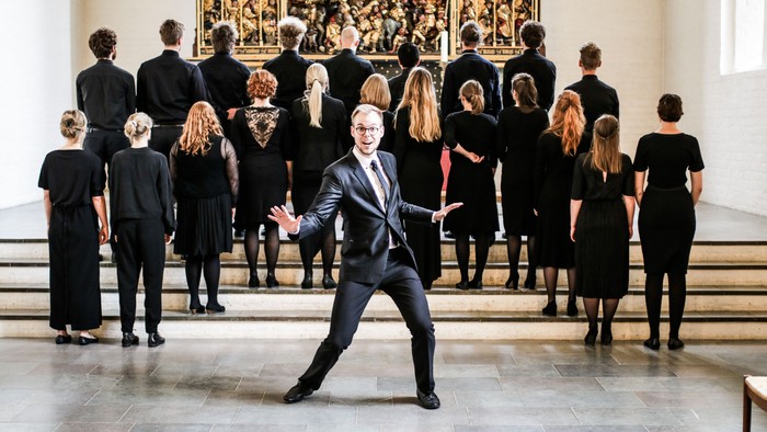 En mand i mørk suite danser i en kirke, omgivet af en gruppe, der ser til.