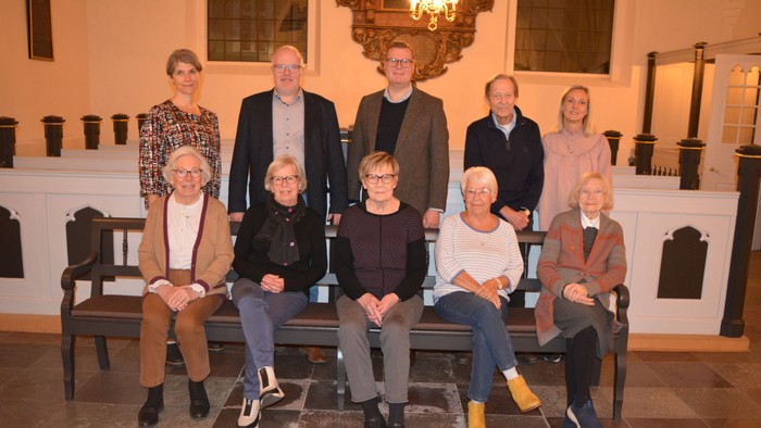 En gruppe af ni personer sidder på en bænk i et historisk rum